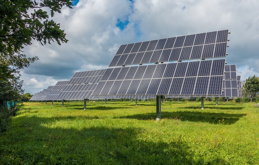 Painéis solares em um campo verde sob um céu parcialmente nublado, representando uma fonte de energia limpa e sustentável.