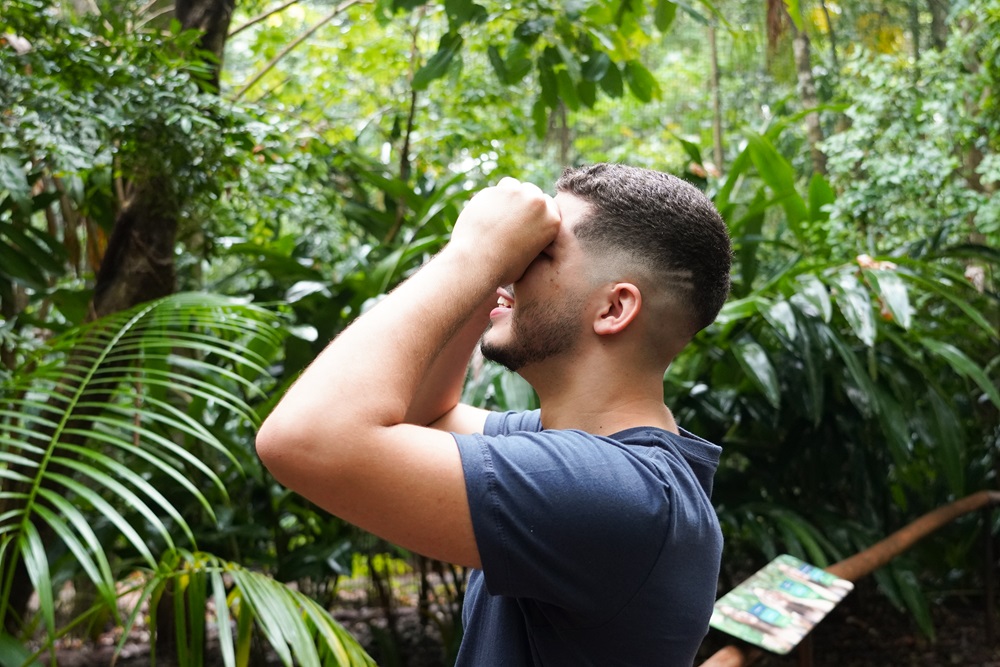 Visitante observando o alto com as mãos em concha nos olhos, em meio à vegetação exuberante do Parque das Aves.