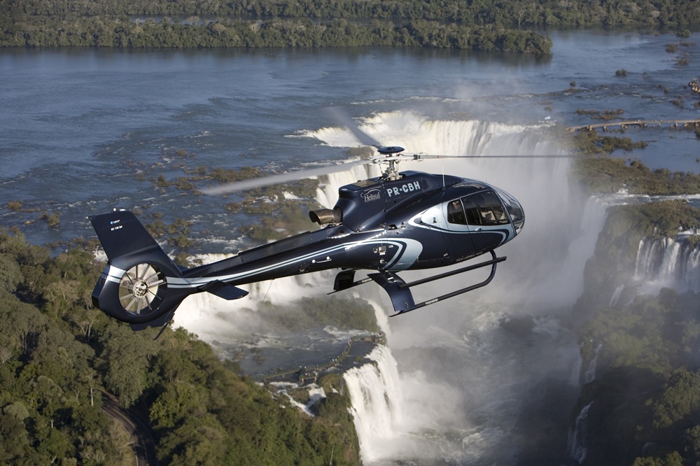 Helicóptero da Helisul Experiência sobrevoando as Cataratas do Iguaçu, proporcionando uma vista panorâmica das quedas d'água cercadas pela floresta exuberante.