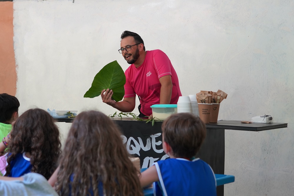 Educador explica sobre a flora da Mata Atlântica, mostrando uma folha de planta para as crianças durante a Colônia de Férias de Janeiro do Parque das Aves, 2024