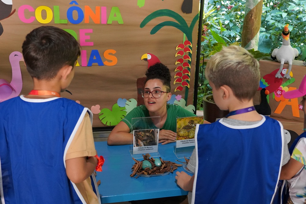 Educadora interage com as crianças, mostrando exemplares de insetos e plantas durante a Colônia de Férias de Janneiro do Parque das Aves, 2024