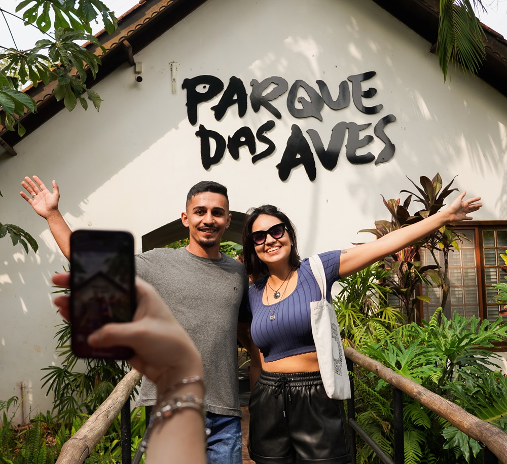 Casal posando na entrada principal do Parque das Aves, sorrindo para uma foto.