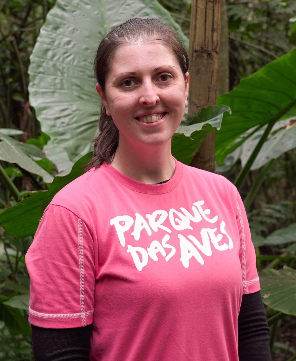 Retrato de uma funcionária do Parque das Aves, sorrindo, veste uma camiseta rosa com o logotipo do Parque das Aves.